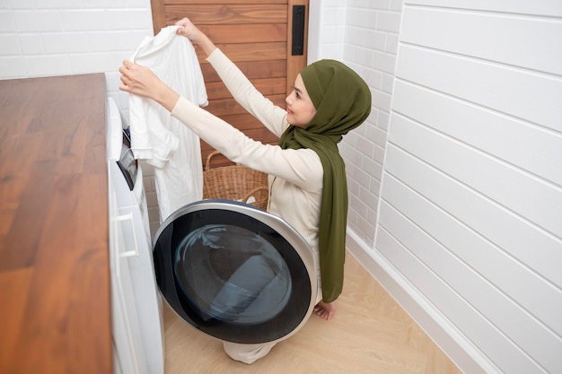 Happy young muslim woman wearing hijab doing laundry in home healthy lifestyle concept