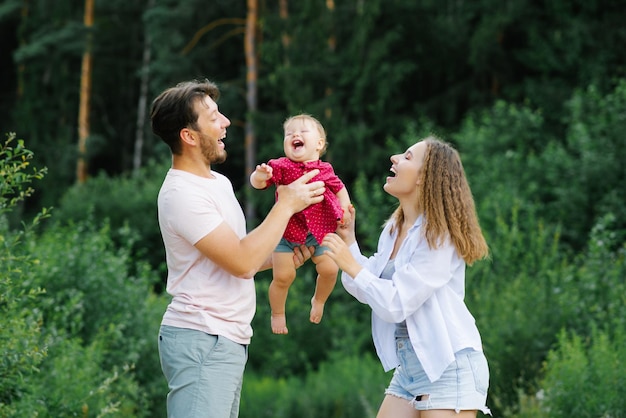 Happy young parents with a baby are walking through the forest having fun and enjoying happy moments