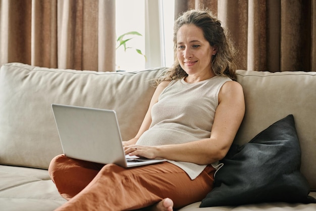 Happy young pregnant businesswoman or female freelancer typing on laptop