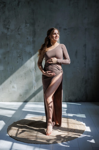 A happy young pregnant woman in a brown delicate suit is posing and stroking her belly Pregnant pregnant woman Happy pregnancy