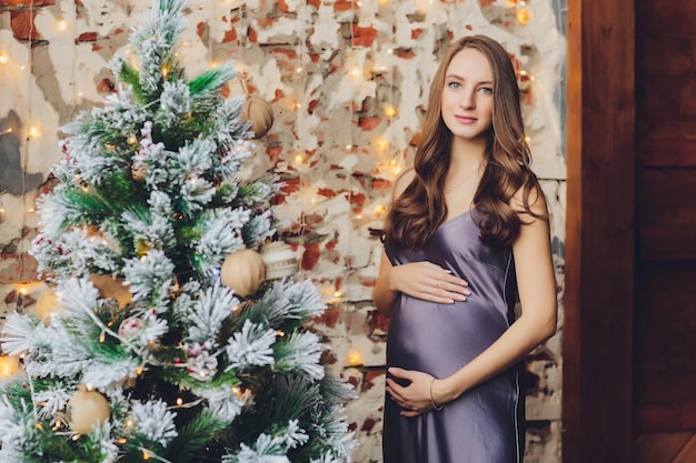 Happy young pregnant woman sitting near the Christmas tree