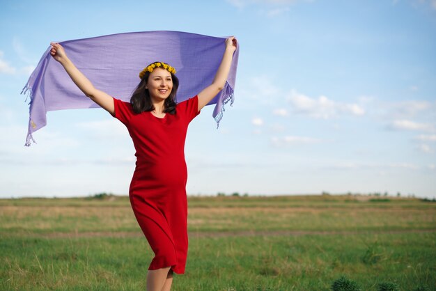 Happy young pregnant woman walking in the fresh air in the afternoon in a red dress.