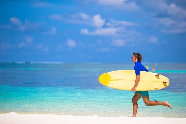 Happy young surf man runing at the beach with a surfboard