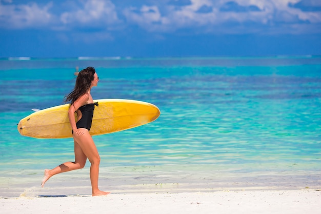 Happy young surf woman runing at the beach with a surfboard