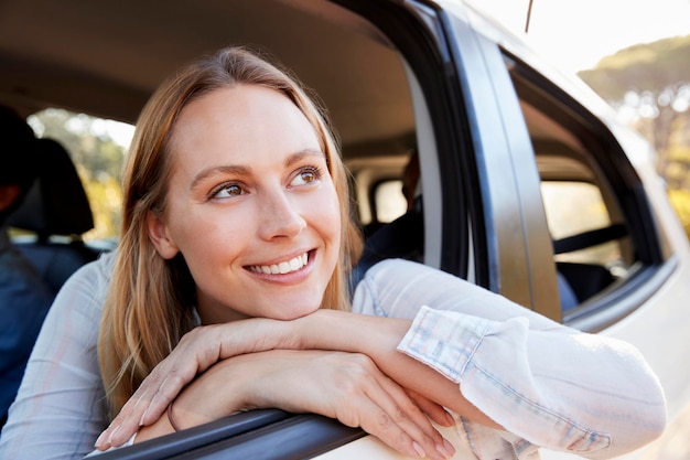 Happy young white woman looking out of a car window smiling