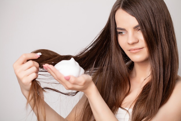 Happy young woman applying hair conditioner in bathroom