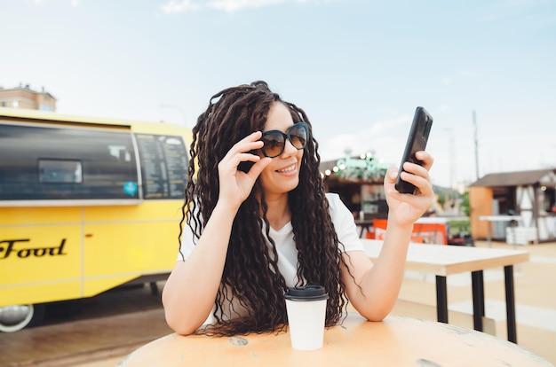 A happy young woman attending a web conference through headphones or a freelancer sitting at an outdoor cafe table a girl with dreadlocks communicates via video link