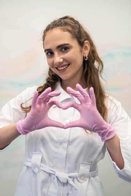 Happy young woman doctor in medical uniform showing heart love gesture or sign