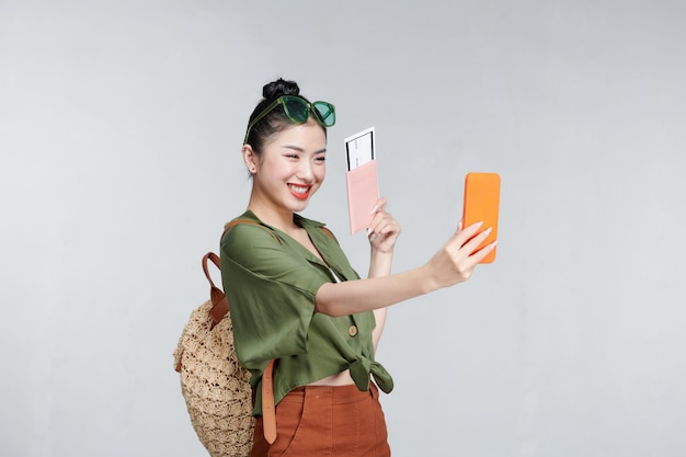 Happy young woman doing selfie while holding passport and flight tickets