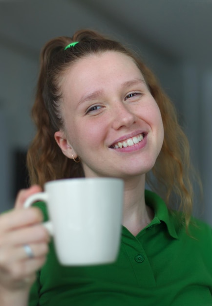 Happy young woman drinking a cup of tea dreaming girl sitting in living room with cup of hot coffee