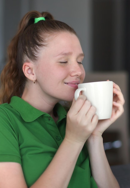 Happy young woman drinking a cup of tea dreaming girl sitting in living room with cup of hot coffee