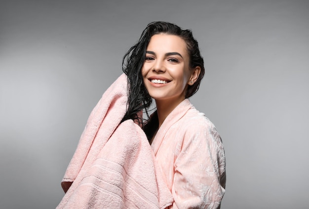 Happy young woman drying hair with towel after washing on light grey background