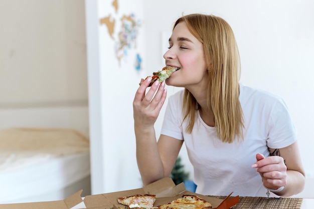 Happy young woman eating a piece of hot pizza at home and enjoying a delicious meal