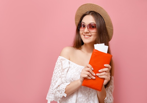 Happy young woman in hat with plane tickets on pink background