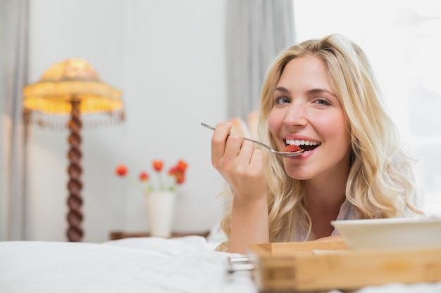 Happy young woman having food in bed