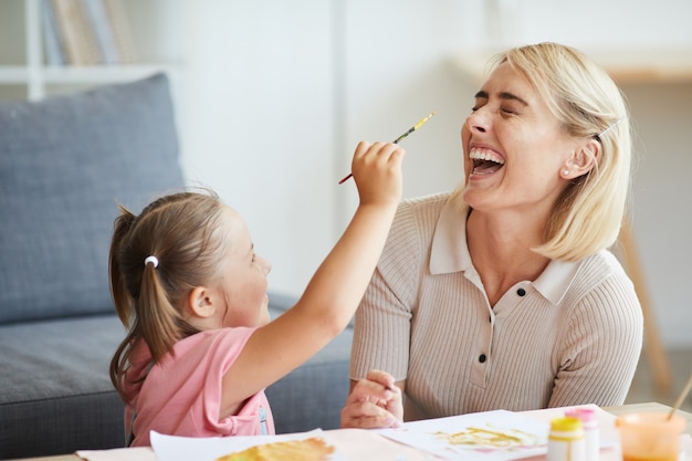 Happy young woman having fun with child during painting with paints in the room