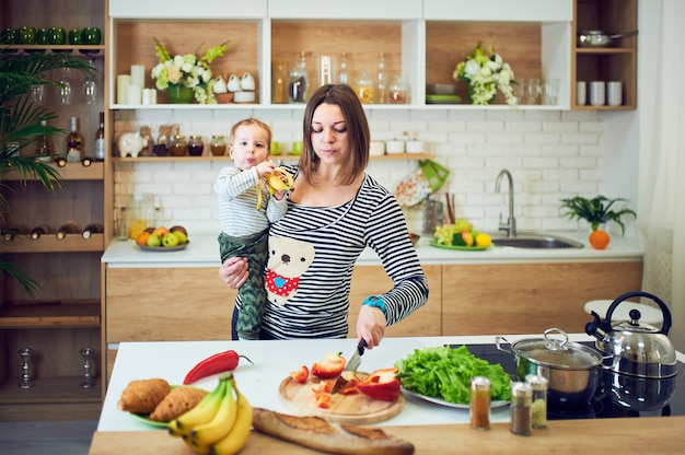 Happy young woman holding a 1 year old child and cooking together in the kitchen