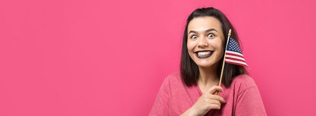 Happy young woman holding American flag against a studio pink background