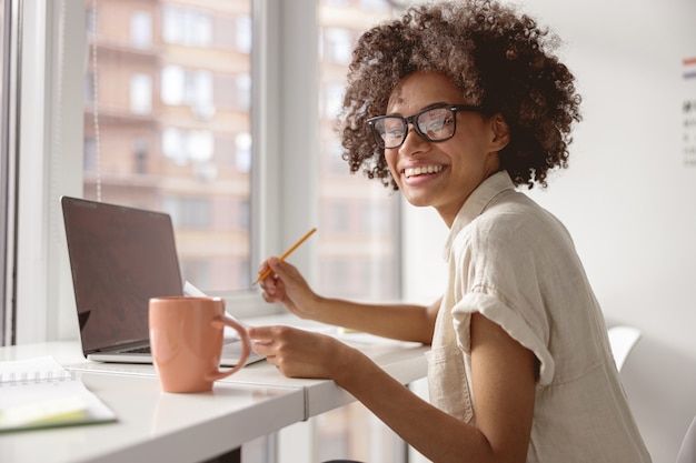 Happy young woman holding document while working near window