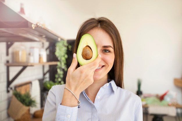 Happy young woman holding half an avocado healthy food foreground focus