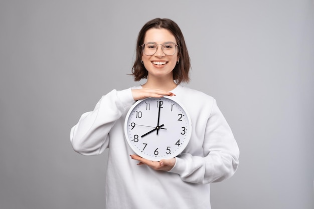 Happy young woman is holding a white clock with both hands