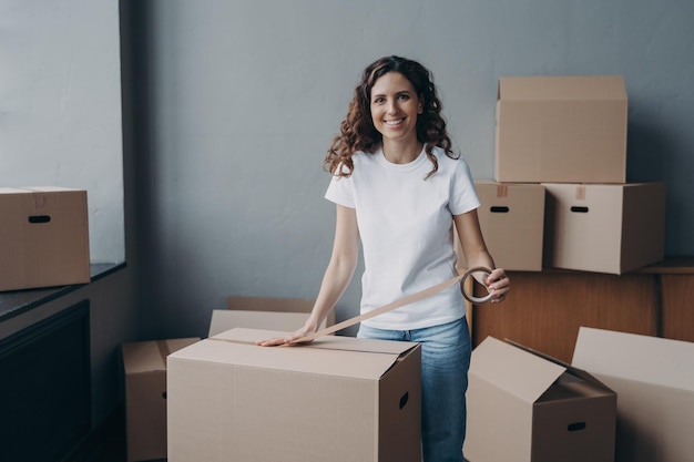 Happy young woman is packing boxes with duct tape Moving service worker preparing cargo