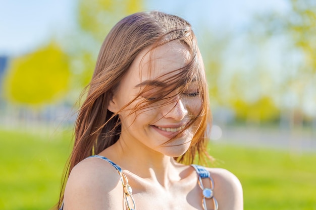 Happy young woman in park Close up portrait beautiful girl windblown hair