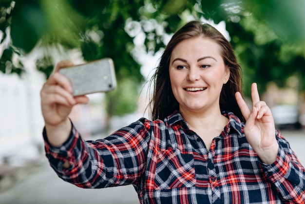 Happy young woman in the park making selfie by camera.