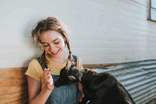 Happy young woman playing with a black baby goat