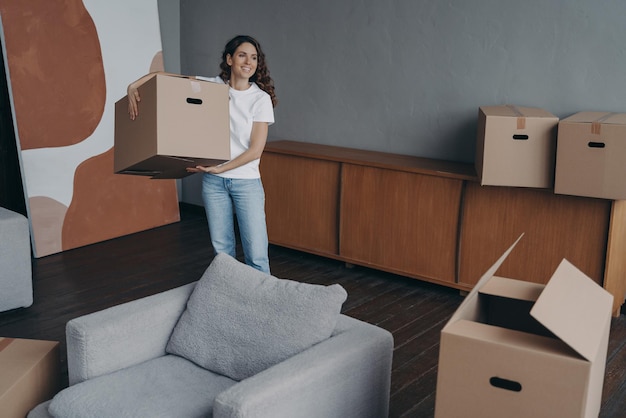 Happy young woman relocates alone and carrying a box Single spanish lady moves