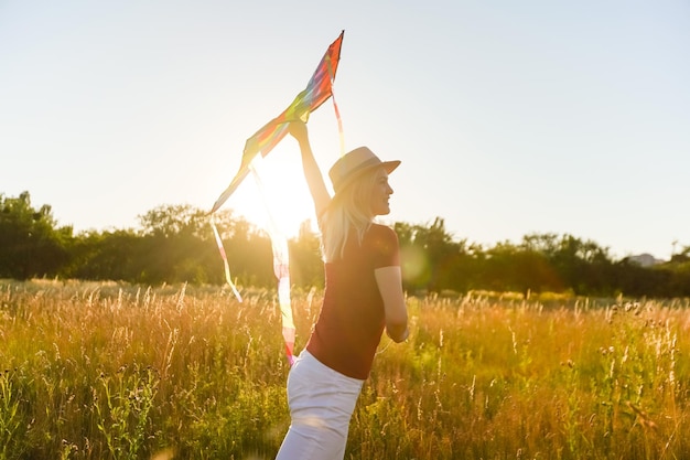 Happy young woman running with a kite on a glade at sunset in summer