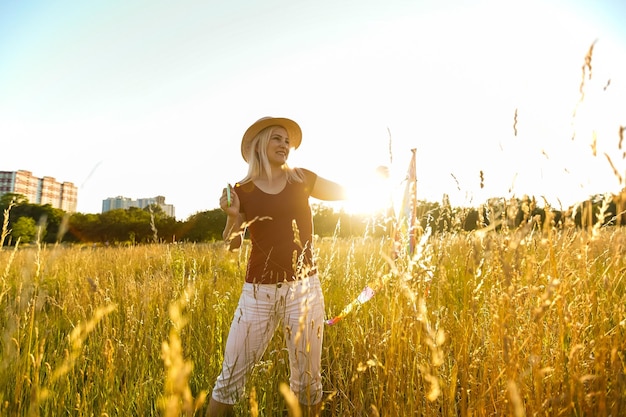 Happy young woman running with a kite on a glade at sunset in summer