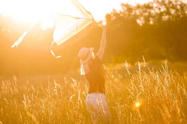 Happy young woman running with a kite on a glade at sunset in summer