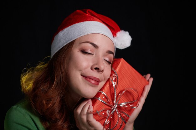 Happy young woman in Santa Hat holding a Christmas present box