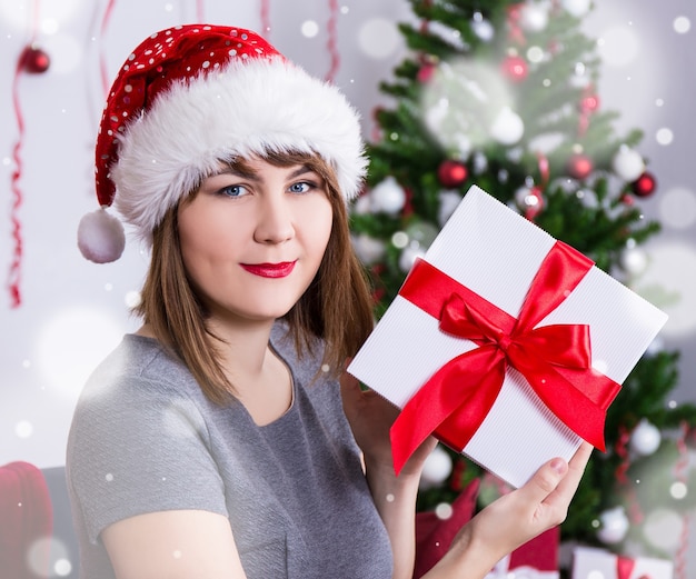 Happy young woman in santa hat with gift box near decorated christmas tree