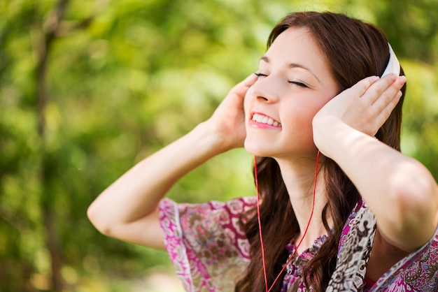 Happy Young Woman sitting on grass in the Beautiful Nature and Listening Music from digital tablet.