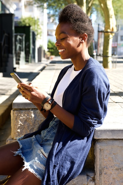 Happy young woman sitting outdoors and using cell phone