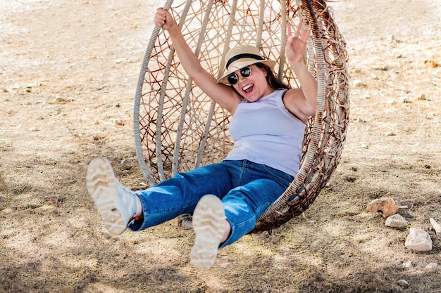 Happy young woman sitting in wicker hanging egg chair in a park