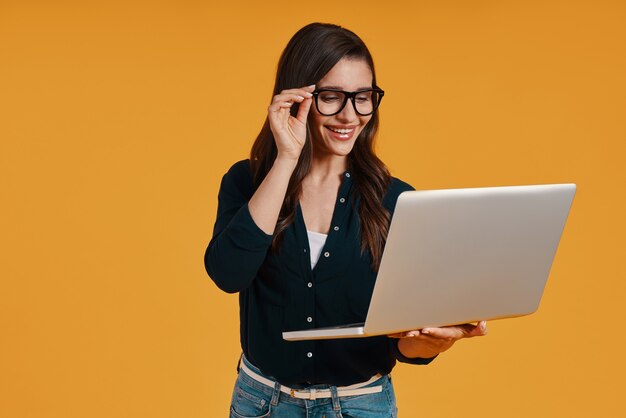 Happy young woman in smart casual clothing using laptop and smiling