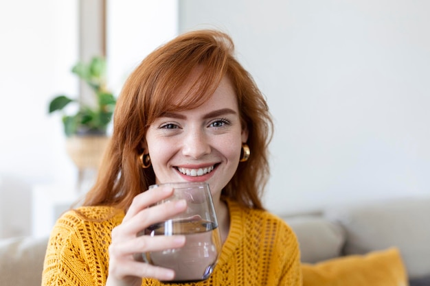 Happy young woman smiling while holding a glass of water at home