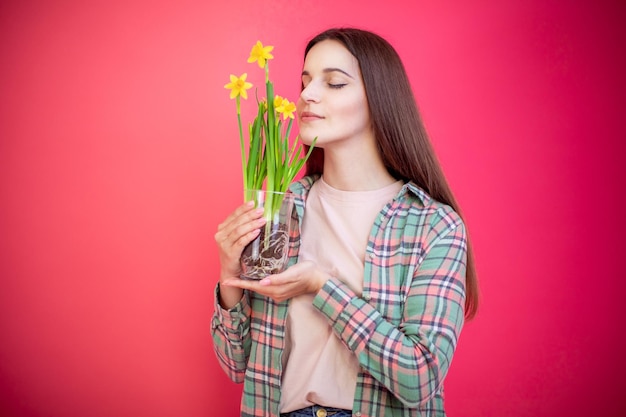 Happy young woman sniffing narcissus plant on pink background