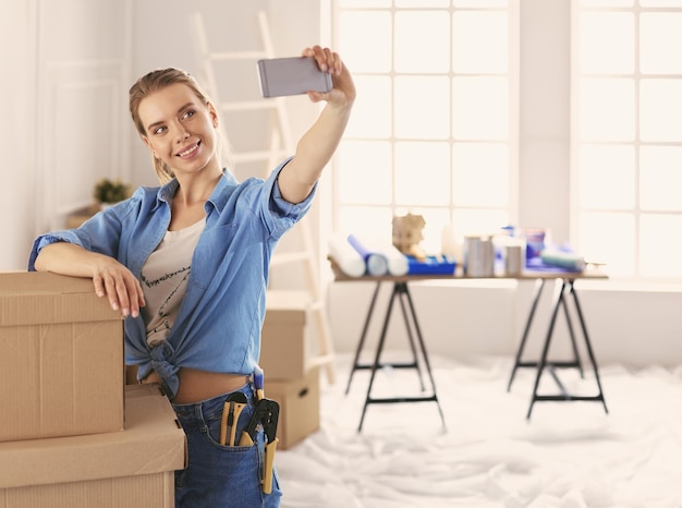 Happy young woman taking selfie while smiling cheerfully having moved into a new flat