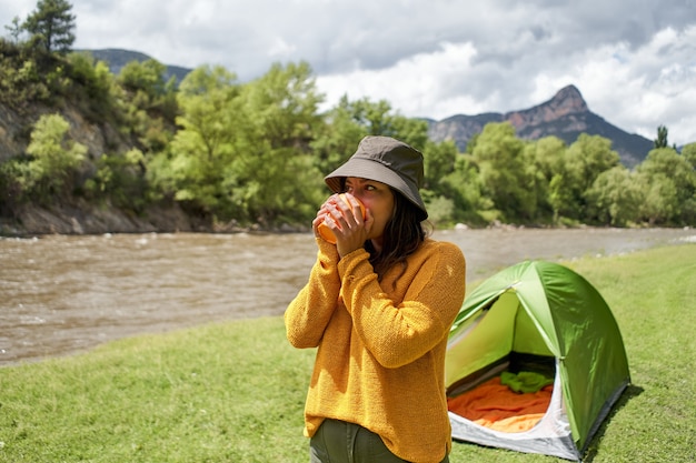 Happy young woman in the tent drinking warm tea or coffee camping in the mountains adventure