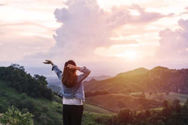 Happy young woman traveler relaxing and looking at the beautiful sunset on the top of mountain