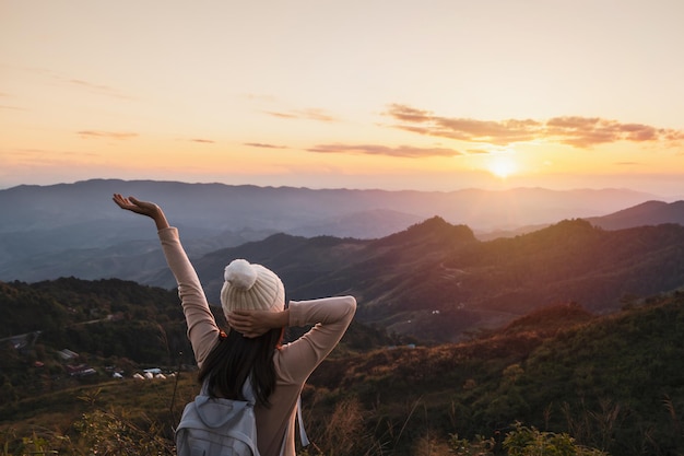 Happy young woman traveler relaxing and looking at the beautiful sunset on the top of mountain