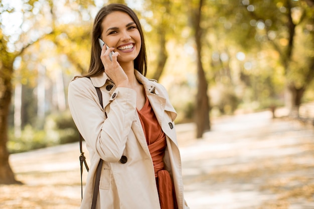 Happy young woman using cell phone in autumn park on beautiful day