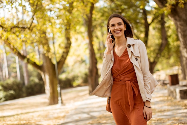 Happy young woman using cell phone in autumn park