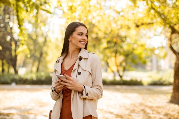 Happy young woman using cell phone in autumn park