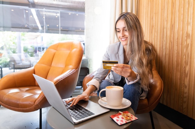 Happy young woman using credit card to buy online in a cafe. Online shopping addiction