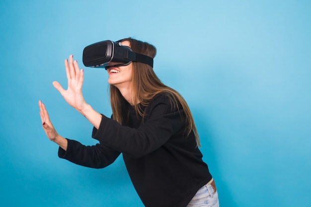 Happy young woman using a virtual reality headset on blue